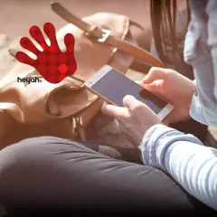 Kobieta z telefonem w dłoniach, obok brązowa torba i czerwona dłoń z logo heyah.