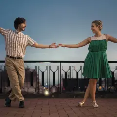 Coppia balla con gioia, un uomo e una donna in abiti retrò, mostrando cos'è lo swing con movimenti aggraziati al tramonto.