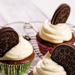 Drei leckere Oreo Muffins mit cremiger Glasur und einem Oreo-Keks obendrauf, auf einem Gitterrost arrangiert.