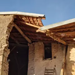 Mise en demeure : mur écroulé du voisin. Bâtiment en ruine, toiture endommagée, ciel bleu.