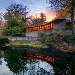 The last Wright house, a modern masterpiece, reflects warmly in a tranquil pond amidst autumn foliage.