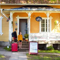 Två personer med resväska anländer till Hajstorp Vandrarhem. En skylt välkomnar besökare.