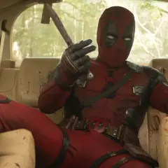 Deadpool, in seinem ikonischen roten Anzug, sitzt lässig im Auto und hält eine blutige Axt. Ein typischer Moment aus den Filmen von Ryan Reynolds.