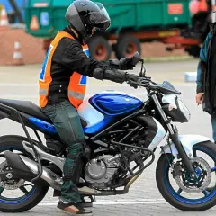 Młody motocyklista w kamizelce odblaskowej na placu manewrowym, obok instruktor. Zastanawia się, od ilu lat prawo jazdy jest wymagane na motocykl.