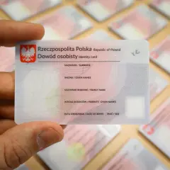 Dłoń trzyma polski dowód osobisty, jeden z wielu leżących na stole. To ważny dokument, zawierający Twój osobisty numer identyfikacyjny.