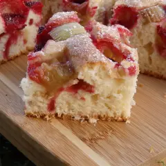 Puszyste ciasto na kefirze z rabarbarem i truskawkami, posypane cukrem pudrem. Idealne na letnie popołudnie.