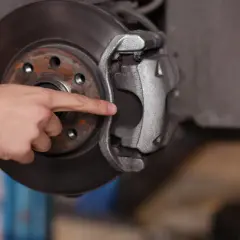 A mechanic's finger points to the dot brake pad thickness, indicating it's time for a replacement.