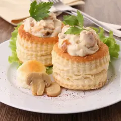 Deux vol-au-vent poulet crémeux, garnis d'une sauce onctueuse et de morceaux de poulet, décorés de persil frais et accompagnés de champignons.