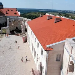 Dziedziniec zamku w Janowcu z ruinami i odrestaurowanym budynkiem z czerwonym dachem.