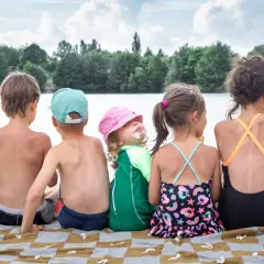 Siedmioro dzieci siedzi na kocu na plaży nad jeziorem, ciesząc się letnim dniem.