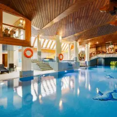 Basen w hotelu Belvedere Resort & Spa z drewnianym sufitem i mostkiem. Woda jest błękitna, a na dnie widoczne są ozdobne ryby.