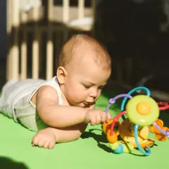 Uroczy 4 miesięczne dziecko leży na macie i bawi się kolorową zabawką.