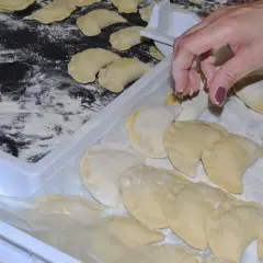 Ręka układa pierogi na tacy, posypanej mąką. Aby ugotowane pierogi się nie skleiły, warto je od razu po ugotowaniu delikatnie polać tłuszczem.
