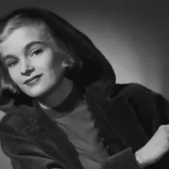 Eva Henning med en cigarett i handen, klädd i en mörk, huva och manchesterjacka.