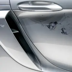 Uszkodzony lakier bezbarwny na srebrnym Porsche GT4. Widoczne odpryski i zacieki wymagające naprawy.