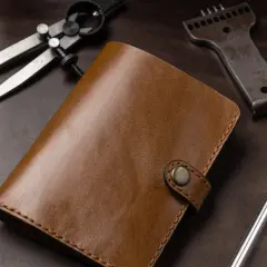 Brązowy portfel ze skóry, narzędzia do obróbki skóry: cyrkiel, dziurkacz, nożyk. Leather cuir to znaczy skóra.