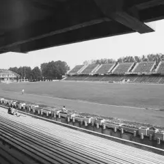 Widok na stary stadion Stali Mielec z pustymi trybunami i boiskiem, gdzie trenuje kilku piłkarzy.