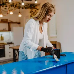 Donna con guanti neri applica vernice blu su un mobile, trasformandolo per rendere opaco un mobile lucido.