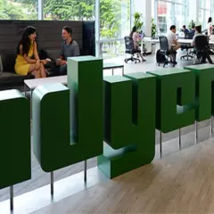Zielone, przestrzenne litery z napisem "adyen" w nowoczesnym biurze. W tle ludzie pracują przy biurkach i rozmawiają.