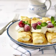 Pyszne naleśniki z mascarpone, udekorowane malinami i miętą, czekają na talerzu. Idealny deser na każdą okazję.