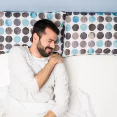 Uomo a letto con dolore alla spalla, dormire con le braccia alzate non è comodo.