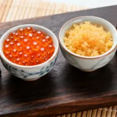 Dwa sushi rolki z ikrą łososia i miseczki z ikrą łososia (tobiko) i ikrą ryb latających.