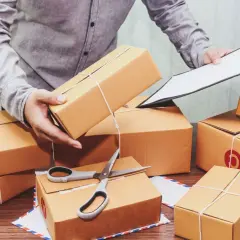 Przygotowanie paczek do wysyłki InPost za pobraniem, kiedy pieniądze czekają na odbiór. W tle stosy kartonów, nożyczki i dokumenty.