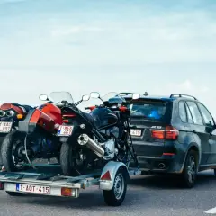 Deux motos sur une remorque tirée par une voiture sur l'autoroute. Le transport de ces véhicules nécessite un permis adéquat pour la catégorie de véhicule tracté.