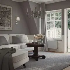 En ljus och luftig salong med sekelskifte inredning. En vit soffa med kuddar, ett runt träbord med blommor och en öppen balkongdörr.