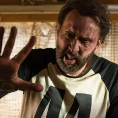 Nicolas Cage med blåmärken och svettig panna, höjer handen i en gest av stopp. En scen från en av hans filmer.