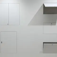 Botole cartongesso invisibili filo muro, integrate perfettamente nella parete bianca, alcune aperte, altre chiuse, nascondono accessi segreti.