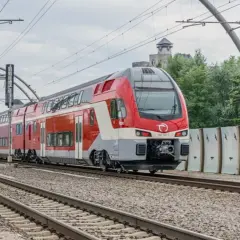 Moderner Doppelstockzug der **Slovak Railways** fährt unter einer Bogenkonstruktion auf Gleisen. Im Hintergrund eine Burg.