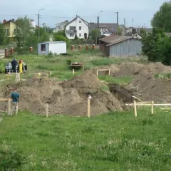 Prace ziemne pod budowę domu. Kopanie fundamentów, hałdy ziemi i pracownicy. Zastanawiasz się, ile kosztuje wykopanie fundamentów pod dom?