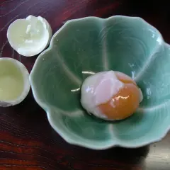 A perfectly soft-boiled egg, a delicacy of Japanese eggs, rests in a green, petal-shaped bowl.