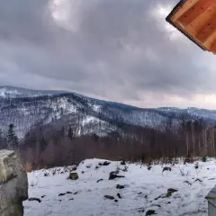 Zimowy krajobraz z ośnieżonymi górami w tle. Na pierwszym planie drewniana altana i kamień. Widok z koziej górki.