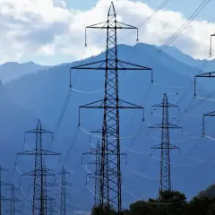 Linie energetyczne na tle gór. Wiele słupów wysokiego napięcia tworzy sieć, która może być wykorzystana w taryfie c12a godziny.