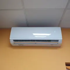Biała jednostka klimatyzacyjna zamontowana na pomarańczowej ścianie pod sufitem podwieszanym.