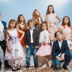 Uśmiechnięte dzieci na weselu, ubrane odświętnie, bawią się wśród konfetti.
