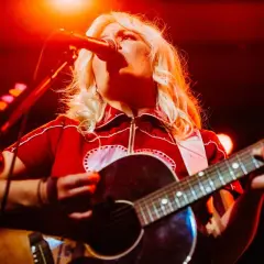 Maja Francis sjunger och spelar gitarr på en scen, upplyst av rött ljus.