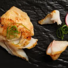 A beautifully grilled saikyo yaki fish fillet, garnished with green onions and a radish slice, rests on a black plate.