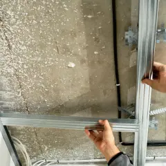 Ręce montują konstrukcję sufitu podwieszanego, łącząc profile aluminiowe. Widać kable i elementy mocujące.