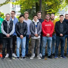Eine Gruppe junger Männer steht lächelnd im Freien. Vielleicht sind sie angehende Fußball-Scouts, die ihre Ausbildung beginnen.