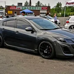 Mörkgrå Mazda 3 med svarta fälgar, redo för en tur. Kanske ett litet **Mazda 3 problem** med däcken?