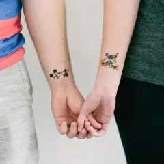 Para trzymająca się za ręce, z tatuażami Myszki Miki na nadgarstkach. Tatuaż myszka miki znaczenie - symbolizuje wieczną przyjaźń i dziecięcą radość.