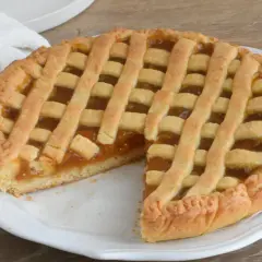 Crostata con marmellata, un classico della crostata ricetta tradizionale, servita su un piatto bianco con un tovagliolo di lino.