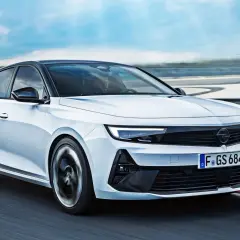 Biały Opel Astra GSe pędzi po torze wyścigowym, z kołami w ruchu, na tle błękitnego nieba.