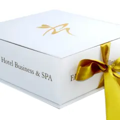 Eleganckie białe pudełko z logo Farmona Hotel Business & SPA, przewiązane złotą wstążką. Idealne na bon do spa.