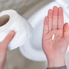 Mano con rotolo carta igienica e capsula bianca, possibile antibiotico per diarrea capre.