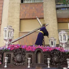Procesión de Semana Santa con imagen de Jesús portando la cruz, adornada con flores y candelabros. Obra de Amadeo Ruiz Olmos.
