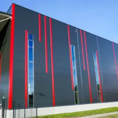 Nowoczesny budynek z szarej płyty warstwowej dachowej, ozdobiony pionowymi czerwonymi pasami i wąskimi oknami.